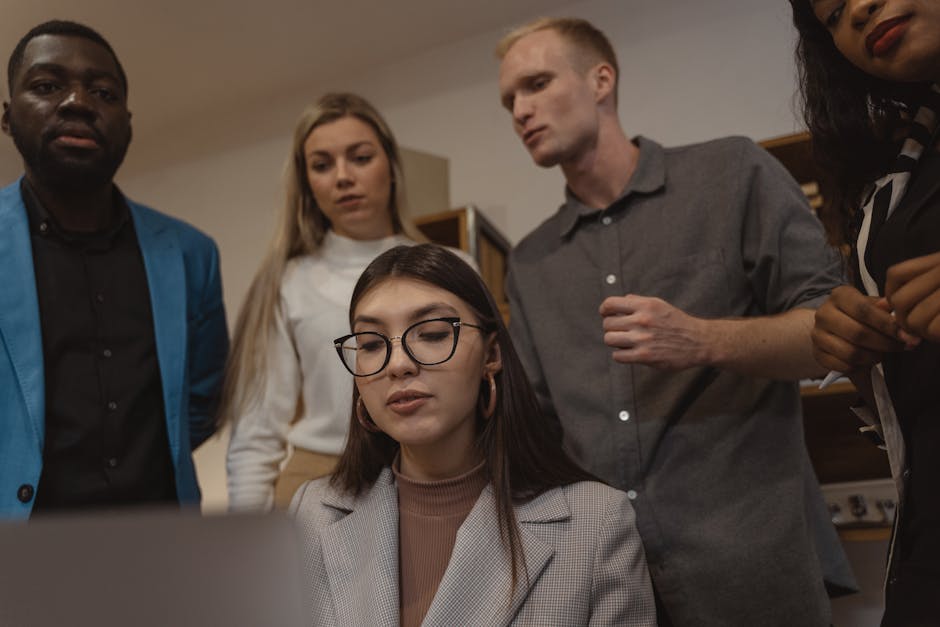A group of professionals in a modern office setting, engaged in teamwork and collaboration around a laptop