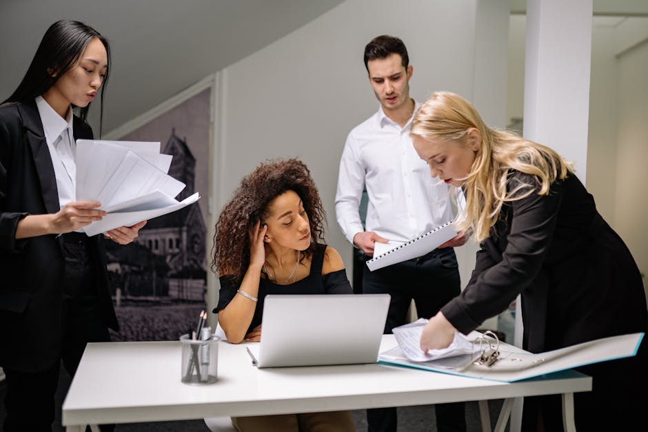 A diverse group of coworkers brainstorming over paperwork and laptops in a corporate office setting