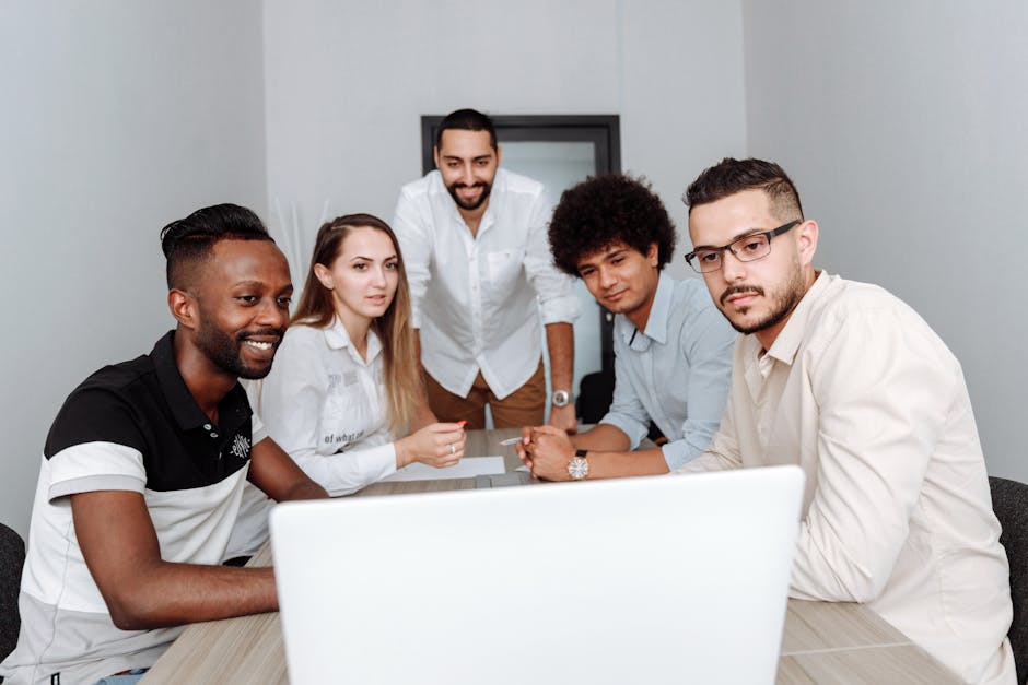 A diverse group of professionals engaging in a collaborative meeting around a laptop in an office.